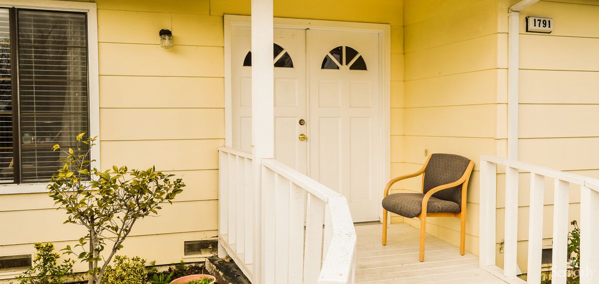 A cozy porch with a chair and a double door on a yellow house.