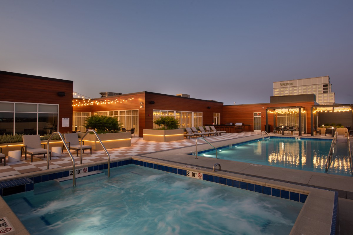 A rooftop swimming pool and hot tub area illuminated during the evening.