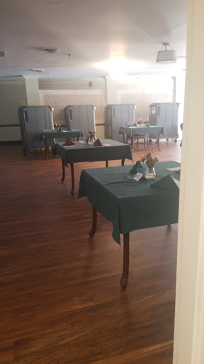 An empty dining area set with green tablecloths, featuring neatly arranged tables and wooden flooring.