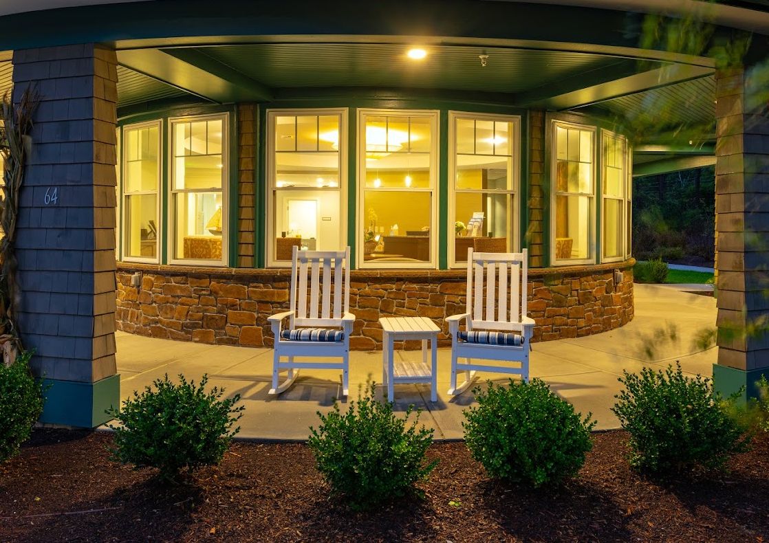 A cozy front porch with two rocking chairs and a small table, warmly lit during the evening.