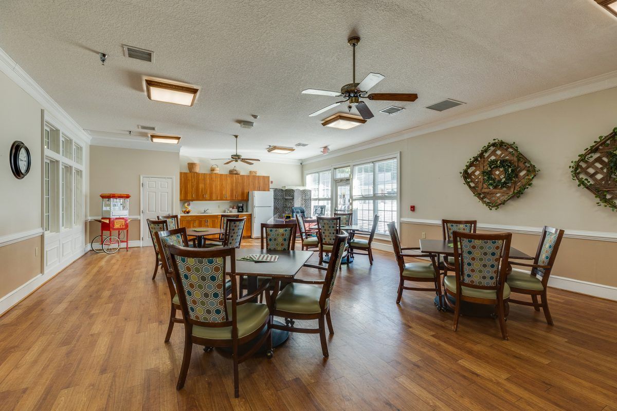 Spacious dining area with multiple tables and chairs, featuring ceiling fans and a kitchen area.