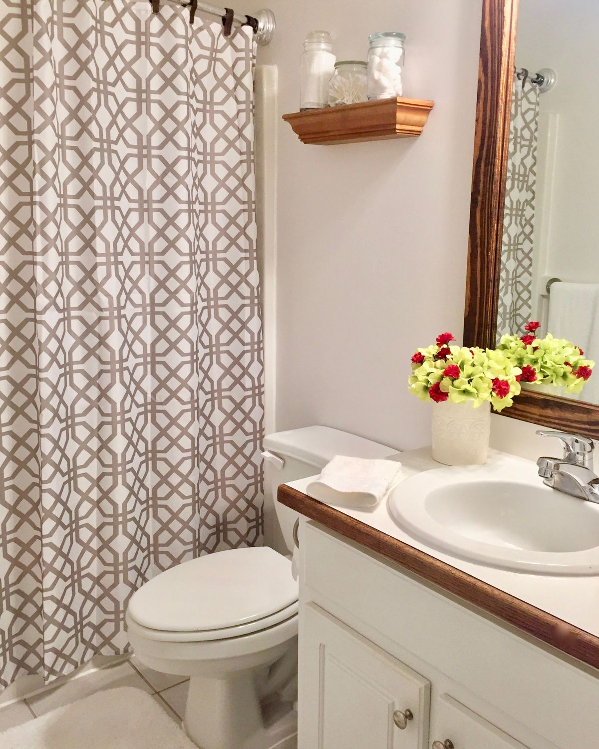 A neatly decorated bathroom with a patterned shower curtain and fresh flowers on the countertop.