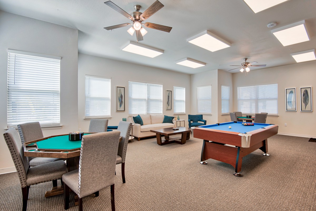 A spacious game room featuring a pool table, seating area, and ceiling fans.