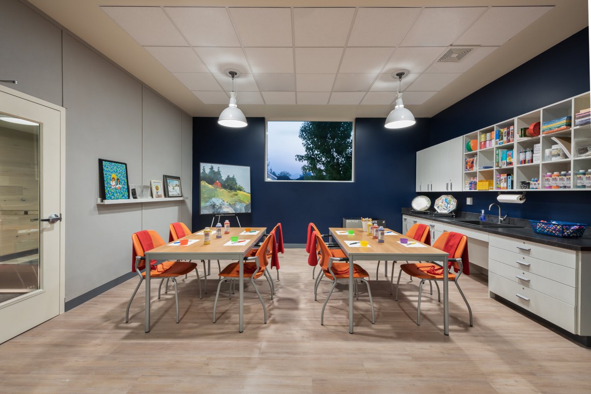 A well-organized classroom with tables and chairs, equipped with art supplies and decorated with posters.