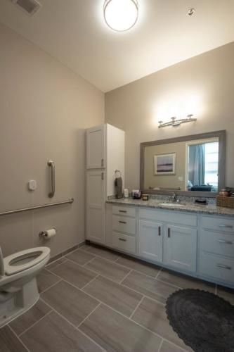 A modern and clean bathroom with a sink, mirror, toilet, and cabinets.