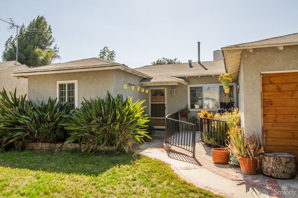 A single-story house with a front yard adorned with plants on a sunny day.