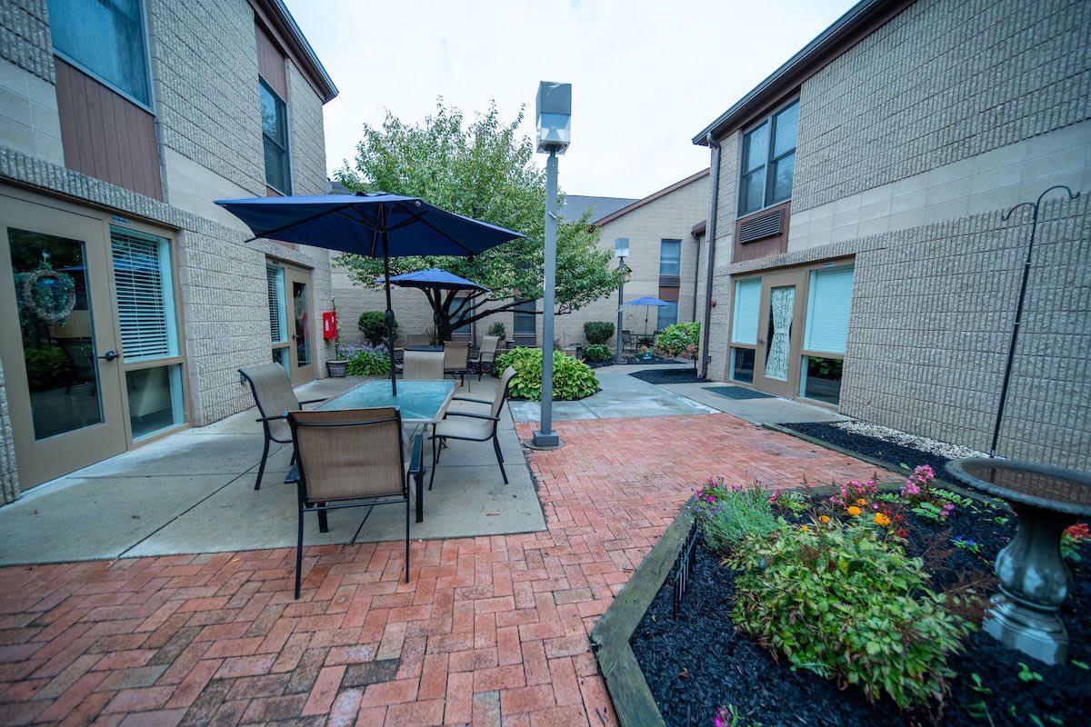 A cozy courtyard with outdoor seating, featuring patio tables and umbrellas surrounded by well-maintained landscaping.