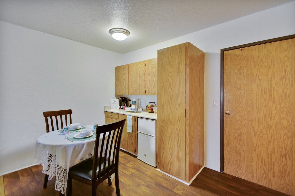 A cozy kitchen and dining area with wooden cabinets, a round table set for a meal, and warm wood flooring.