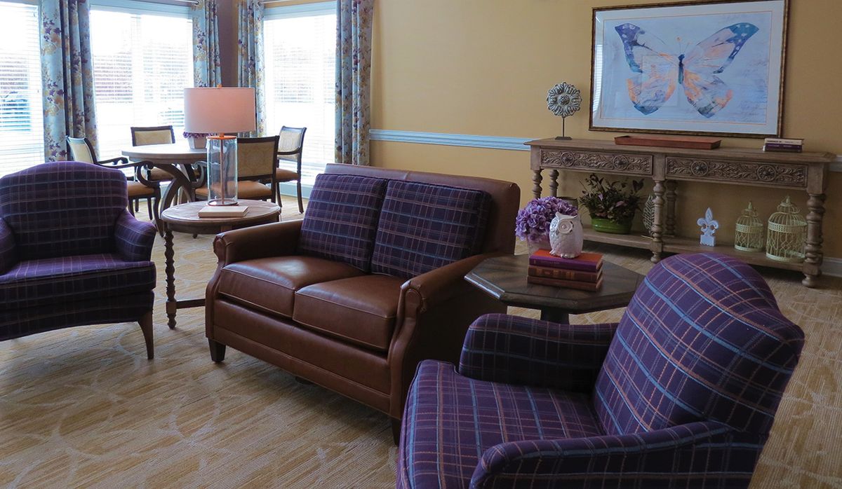 A cozy living room with a brown sofa and purple plaid chairs, featuring a fireplace and tasteful decor.