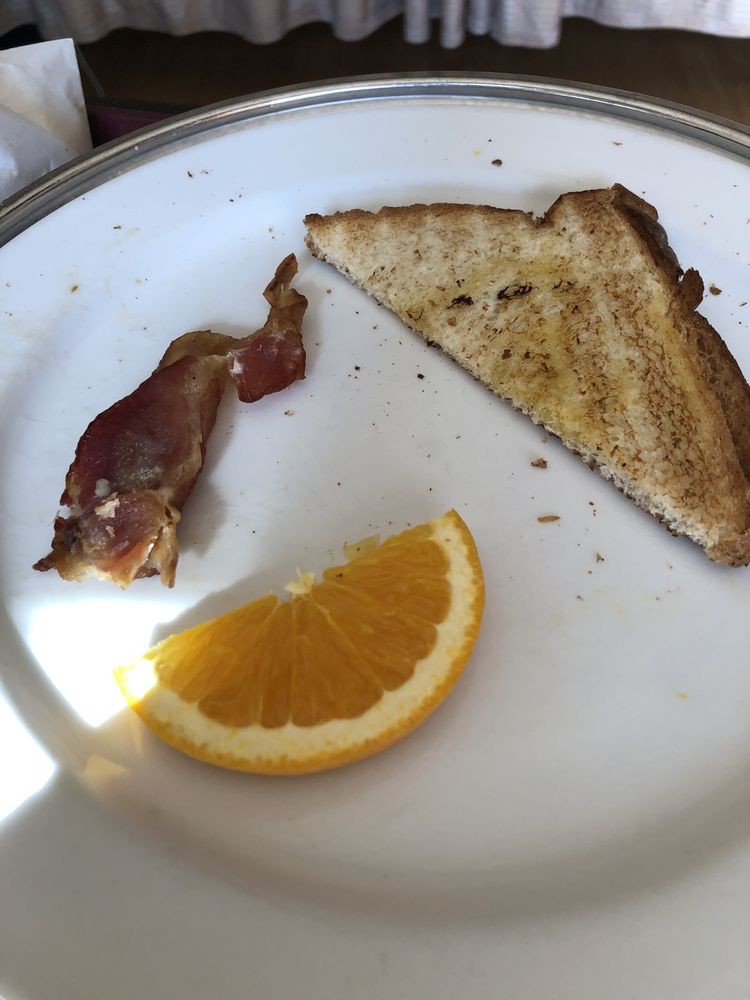 A breakfast plate with a slice of toast, a strip of bacon, and an orange slice.