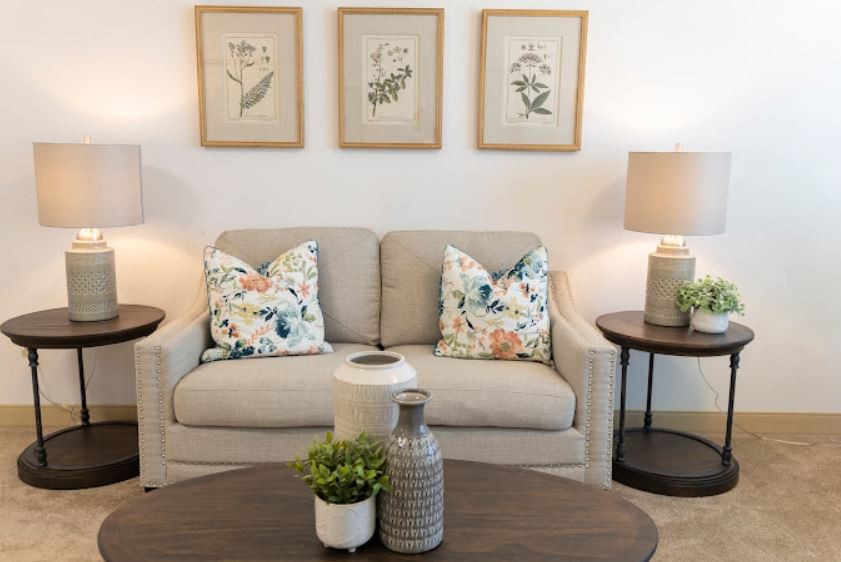A cozy living room with a neutral sofa, floral cushions, and botanical artwork on the wall.