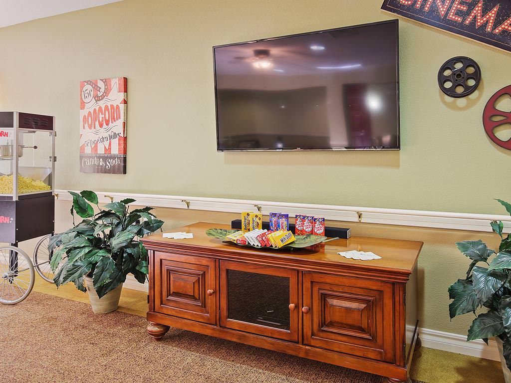 A cozy living room setup featuring a large television mounted on the wall above a wooden cabinet, complemented by decorative plants and wall art.
