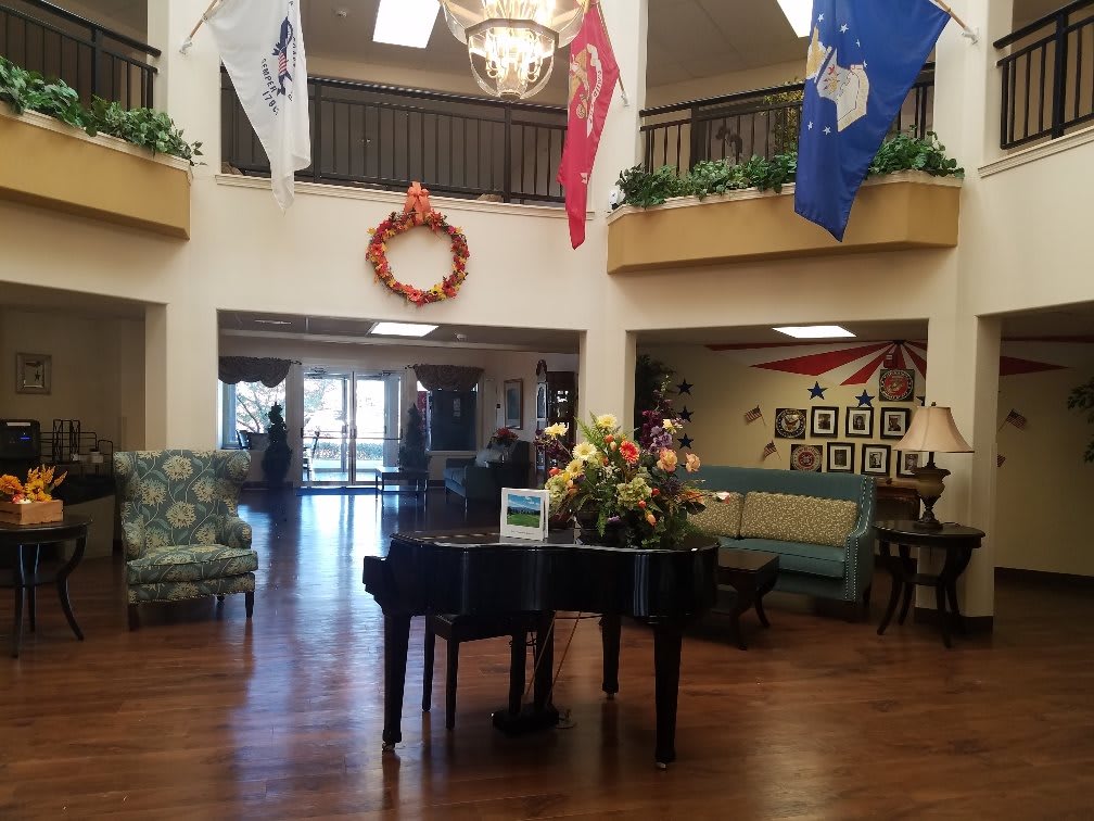 A spacious lobby featuring a grand piano, decorative wreath, flags, and elegant lighting.