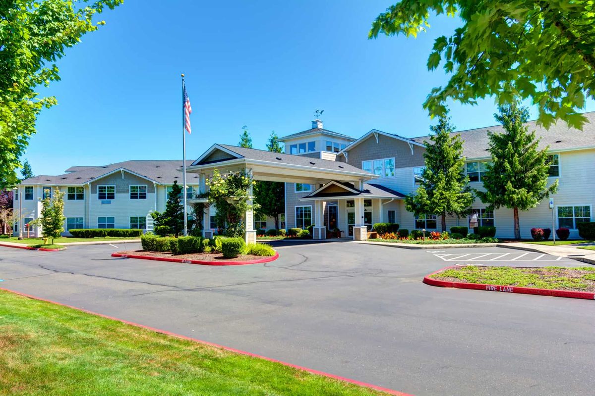 A large building with a driveway, surrounded by trees and a flagpole on a sunny day.
