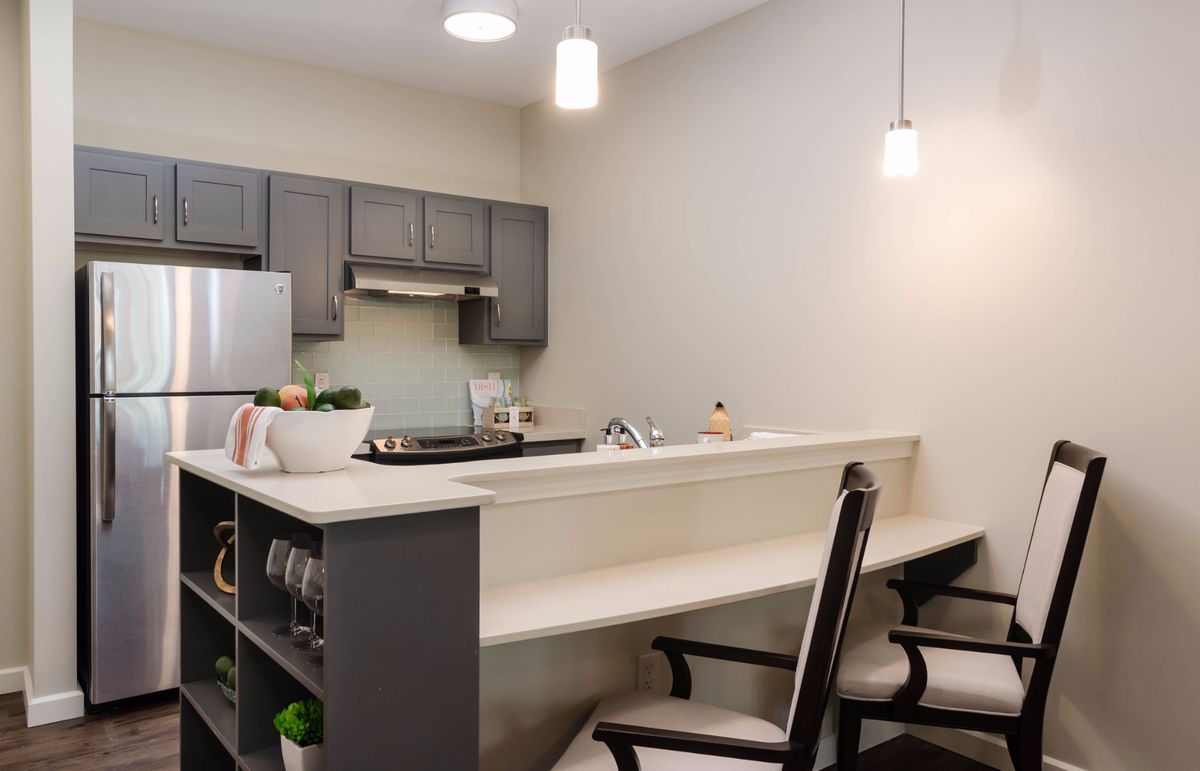 A modern kitchen interior featuring a sleek countertop with chairs and pendant lighting.