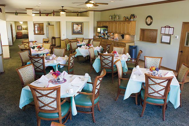 A cozy dining area with neatly arranged tables and chairs, accompanied by a kitchen space.