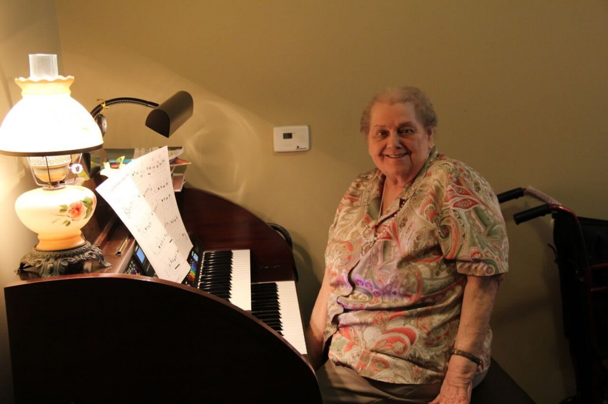 An elderly woman sitting at a piano with sheet music.