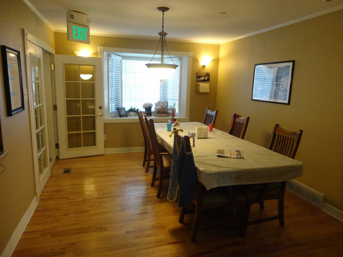A cozy dining room featuring a long table with chairs, wooden flooring, and warm lighting.