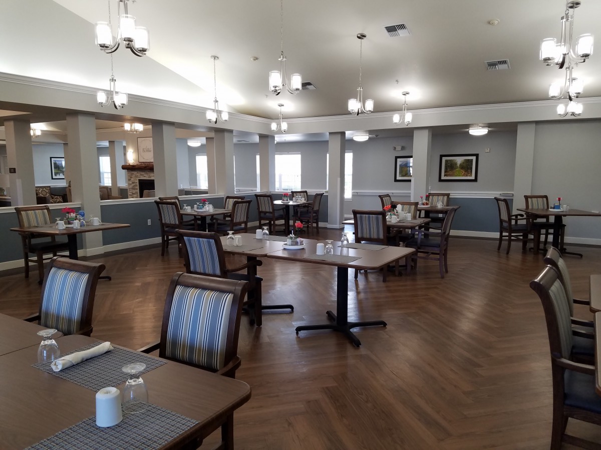 An empty dining area with neatly arranged tables and chairs, featuring elegant lighting and wooden flooring.