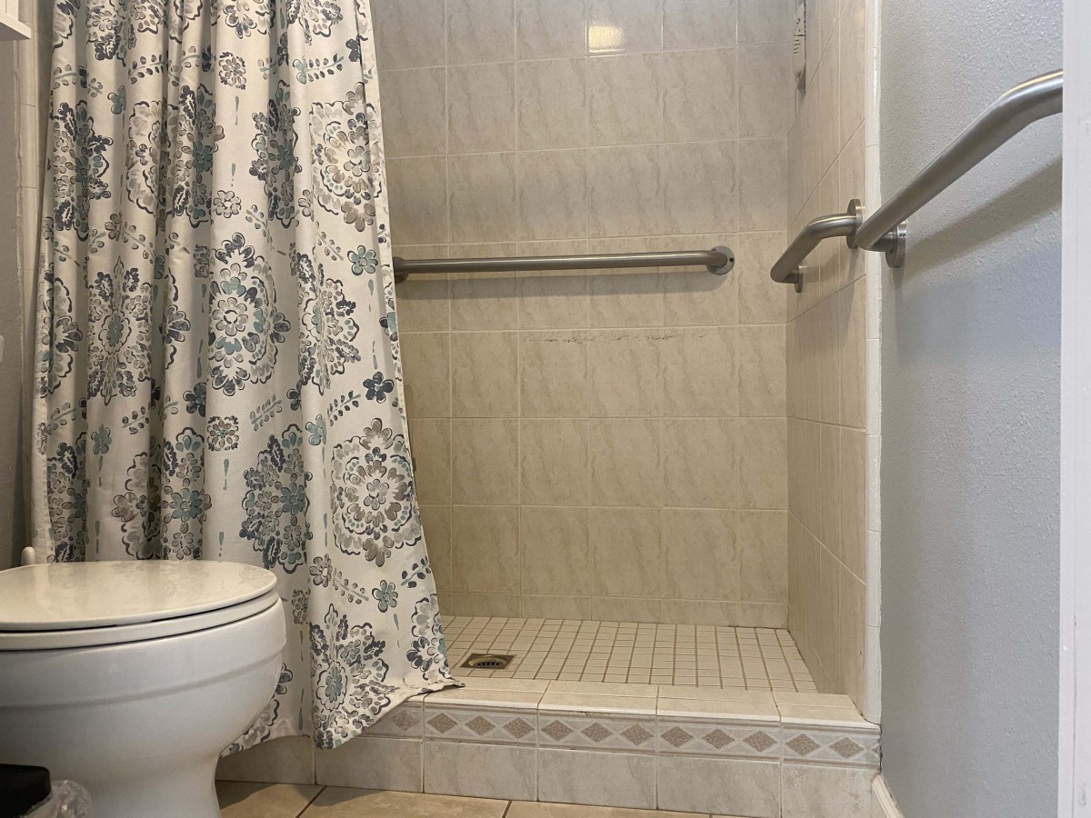 A bathroom with a walk-in shower, featuring decorative curtains and safety grab bars.