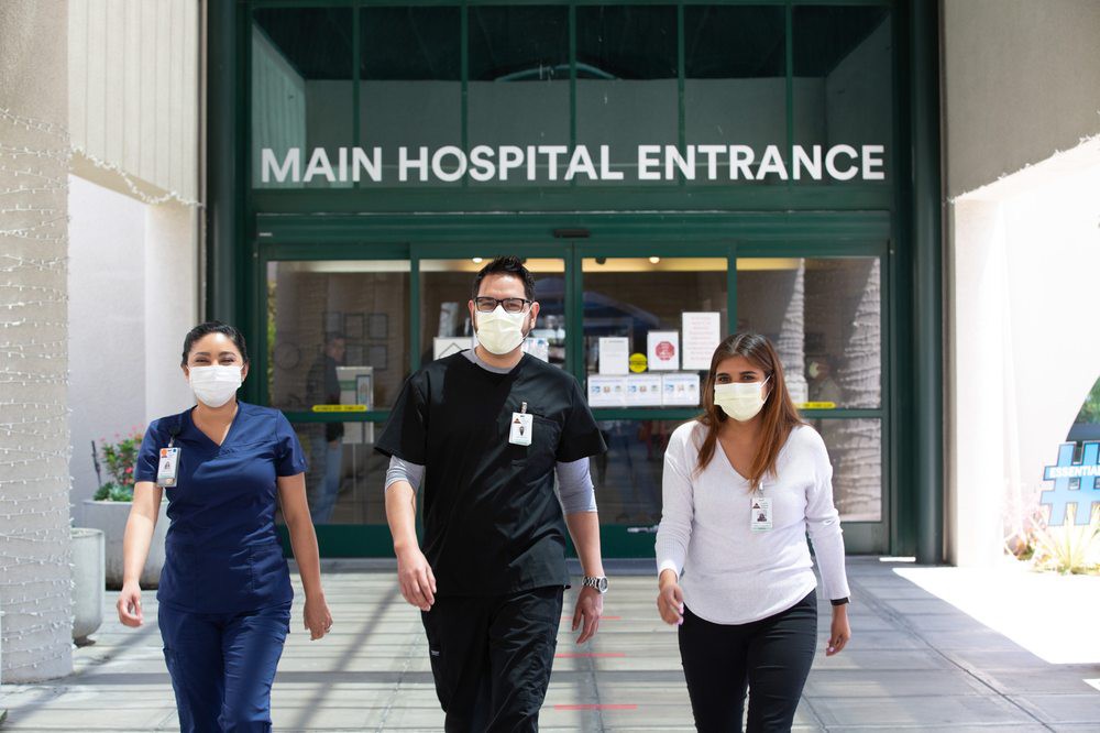 Healthcare workers wearing masks walking out of the main hospital entrance.