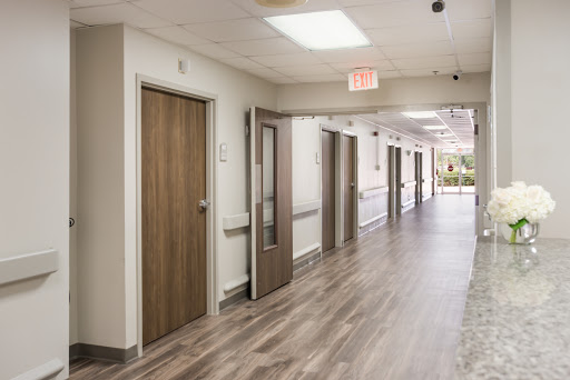 A view of a well-lit hospital hallway featuring wooden doors and modern flooring.