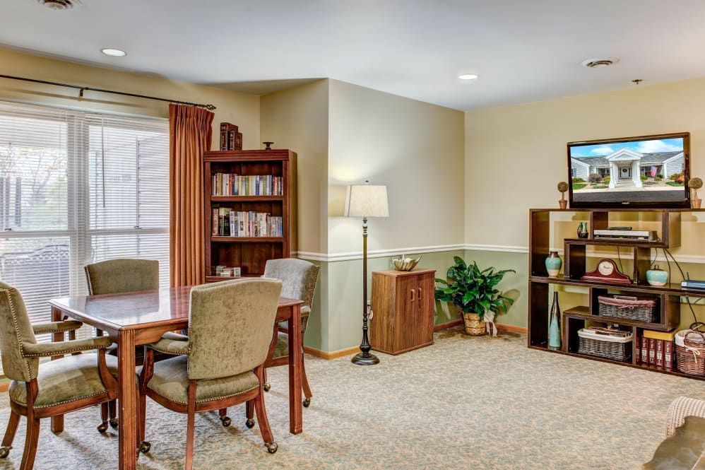 A cozy living room with a bookshelf, table and chairs, a television, and a floor lamp.