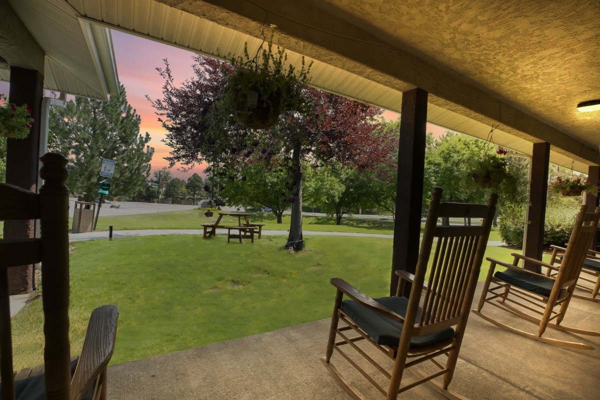A tranquil porch with rocking chairs overlooking a grassy yard at sunset.