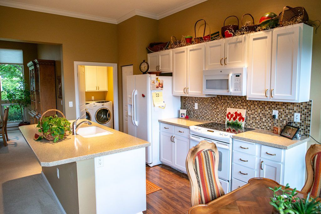 A modern kitchen with white cabinets, a tile backsplash, and wood flooring.