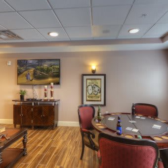 A cozy interior featuring a poker table surrounded by chairs, with artwork on the walls and a wooden floor.