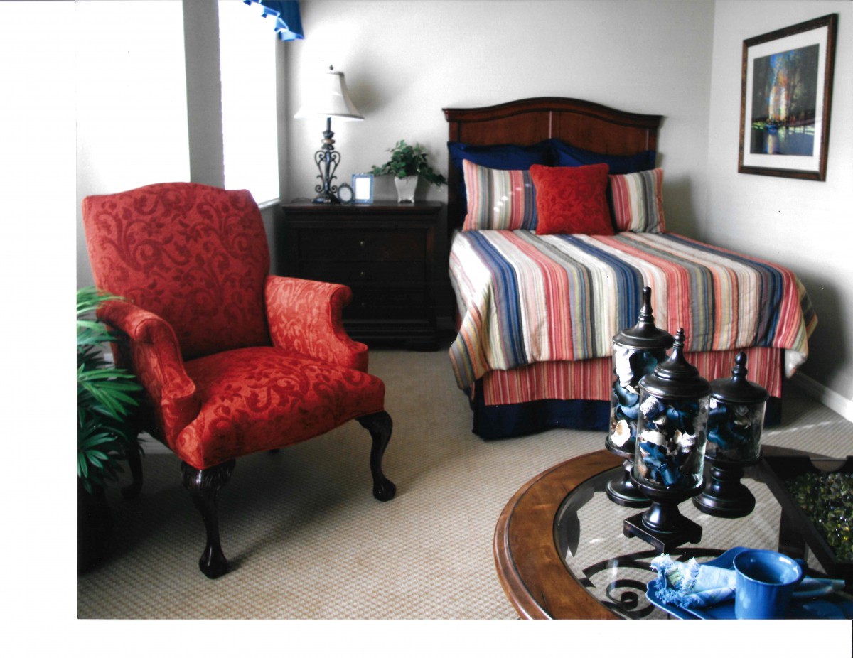 A cozy bedroom with a striped bed, red armchair, and elegant decor.