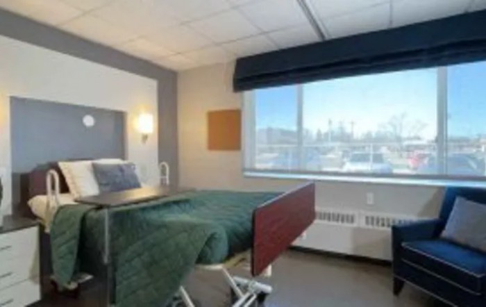 A well-lit hospital room with a bed and a large window overlooking the cityscape.