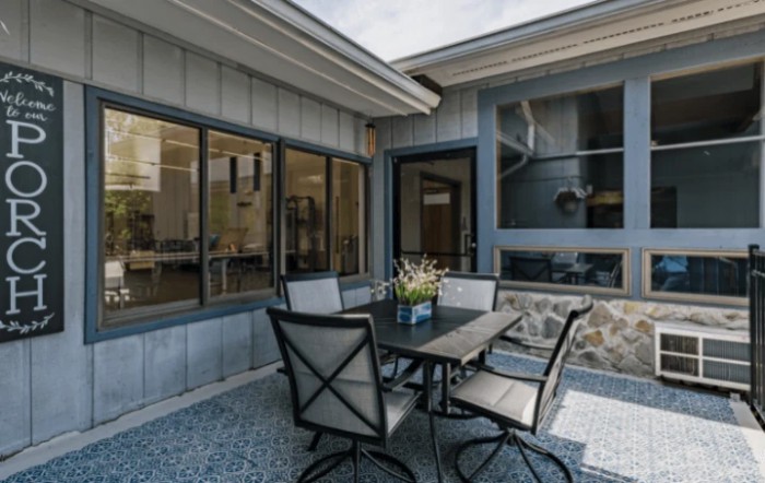A cozy outdoor patio area featuring a dining table with chairs, surrounded by large windows and decorated with a flowerpot.