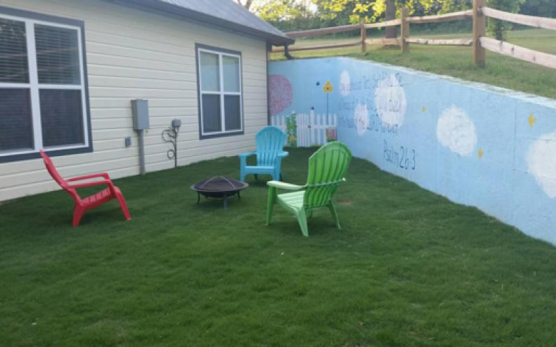 A cozy backyard with colorful chairs, a fire pit, and a mural on the fence.