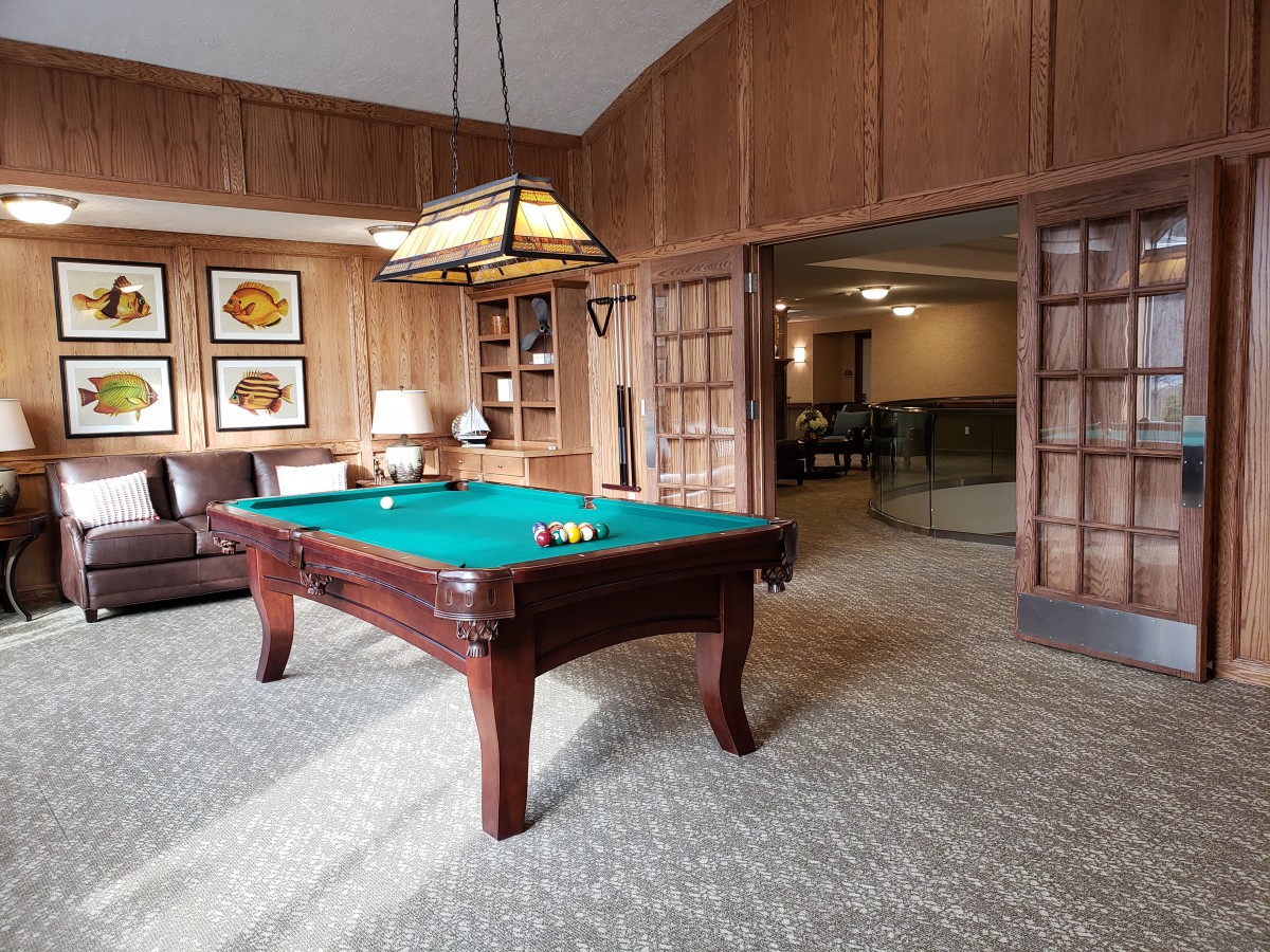 A cozy game room featuring a pool table, leather sofa, and wood paneling.