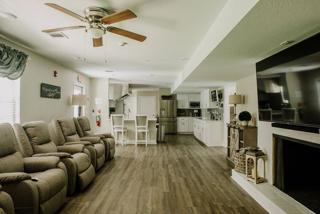 An open floor plan living area with a kitchen, featuring recliner seating and hardwood floors.