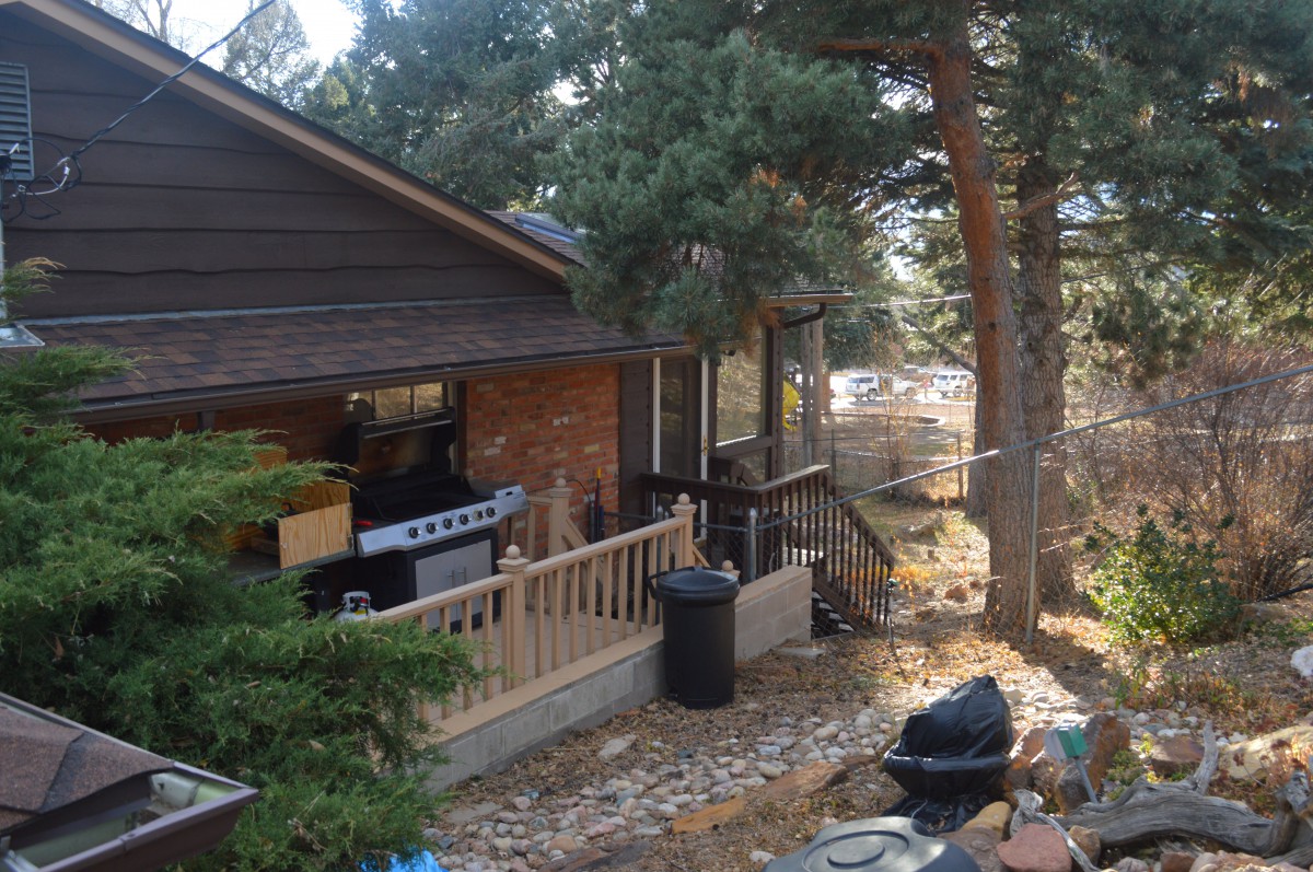 A cozy outdoor patio area with a grill, surrounded by trees.