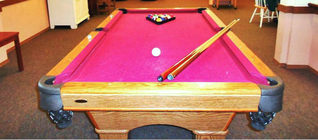 A pink-felt pool table with racked balls and cue sticks ready for play.