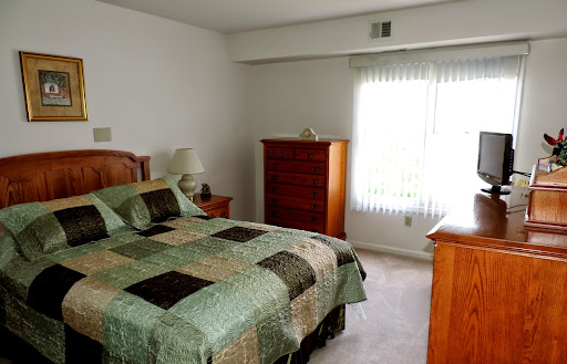 A cozy bedroom featuring a quilted bedspread, wooden furniture, and natural light from a window.