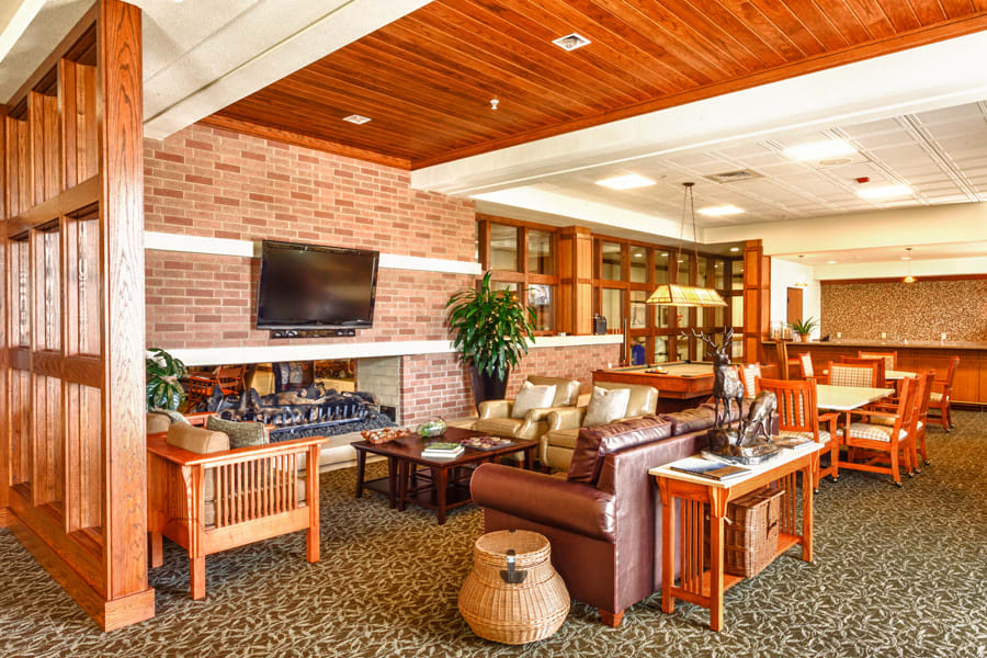A cozy living room with warm wooden accents, featuring a TV, comfortable seating, and decorative plants.