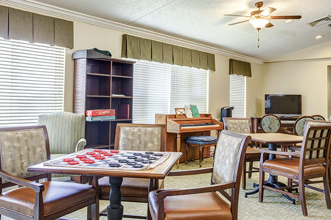 A cozy game room with a checkers board, comfortable seating, and a piano.