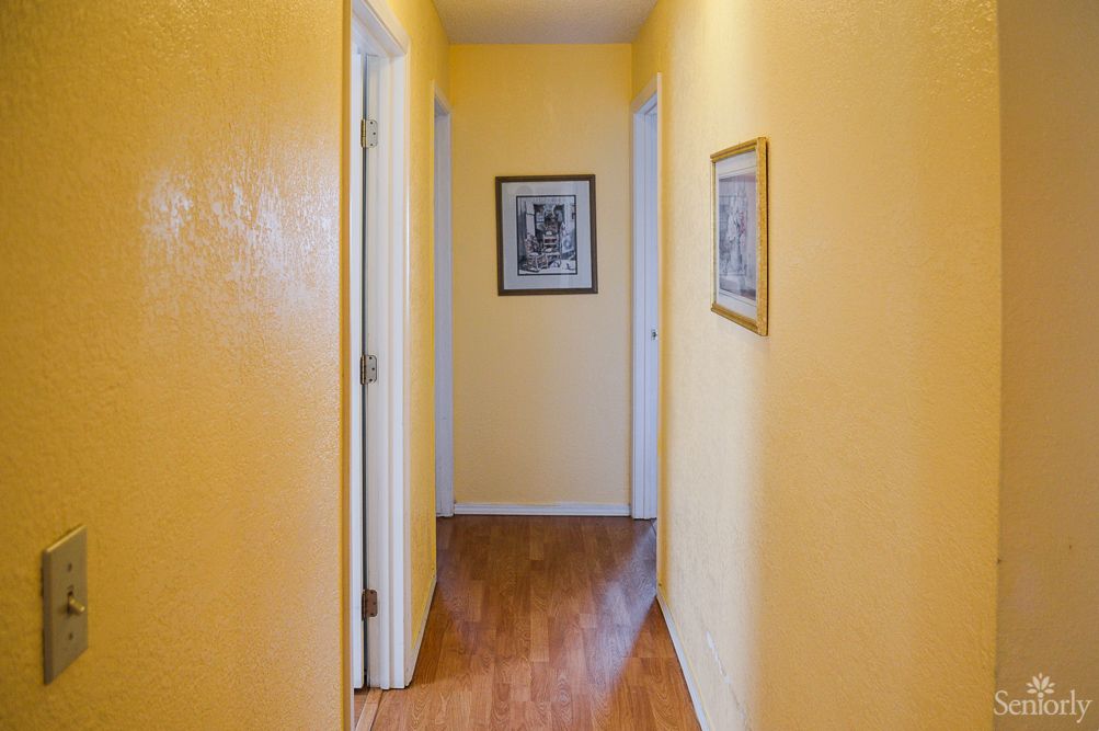 A brightly painted hallway with yellow walls, wooden floors, and framed artwork on the walls.