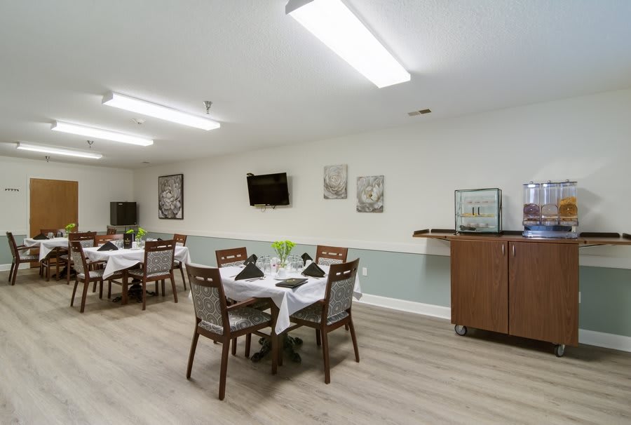 A neatly arranged dining room with tables set for service, featuring modern decor and a television mounted on the wall.