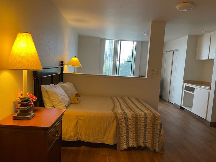 A cozy bedroom featuring a neatly made bed with pillows, bedside lamps, and a window allowing natural light.