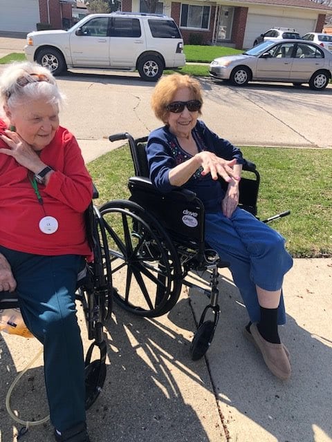Two elderly individuals enjoying a conversation outside in their wheelchairs.