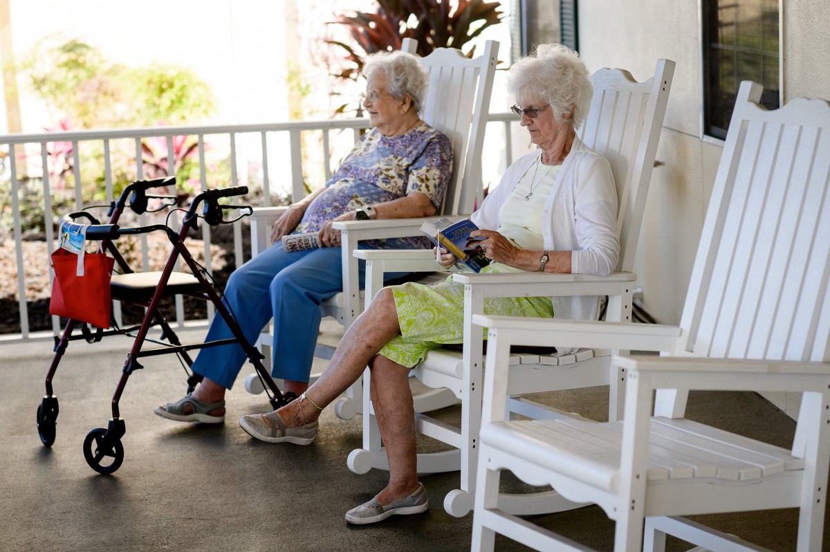 Two elderly women sitting on a porch, one reading a book.