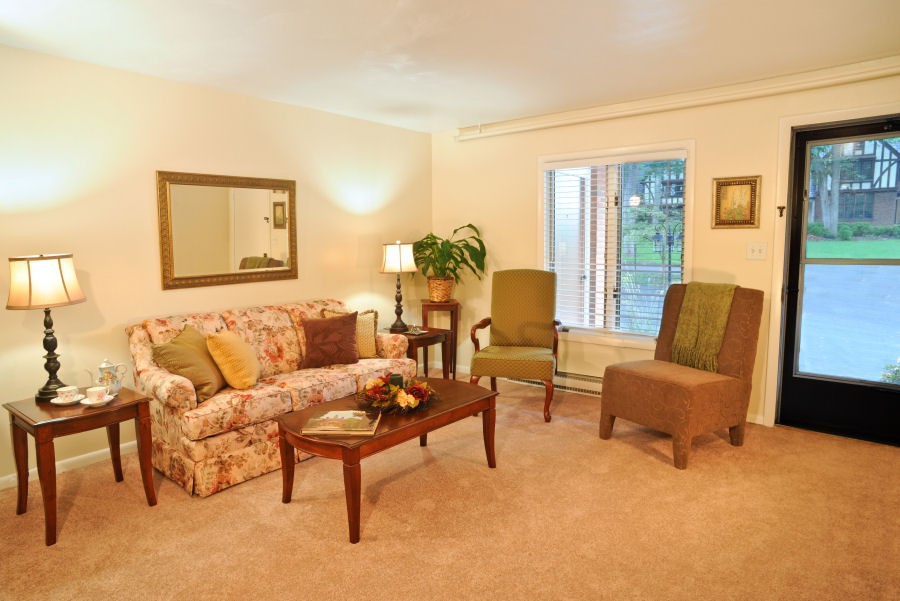 A cozy and warmly lit living room with a floral sofa, two green chairs, a wooden coffee table, and decorative elements.