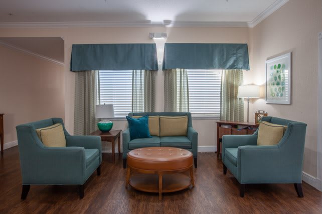 A cozy living room with teal armchairs, a sofa, and a round wooden coffee table under soft lighting.
