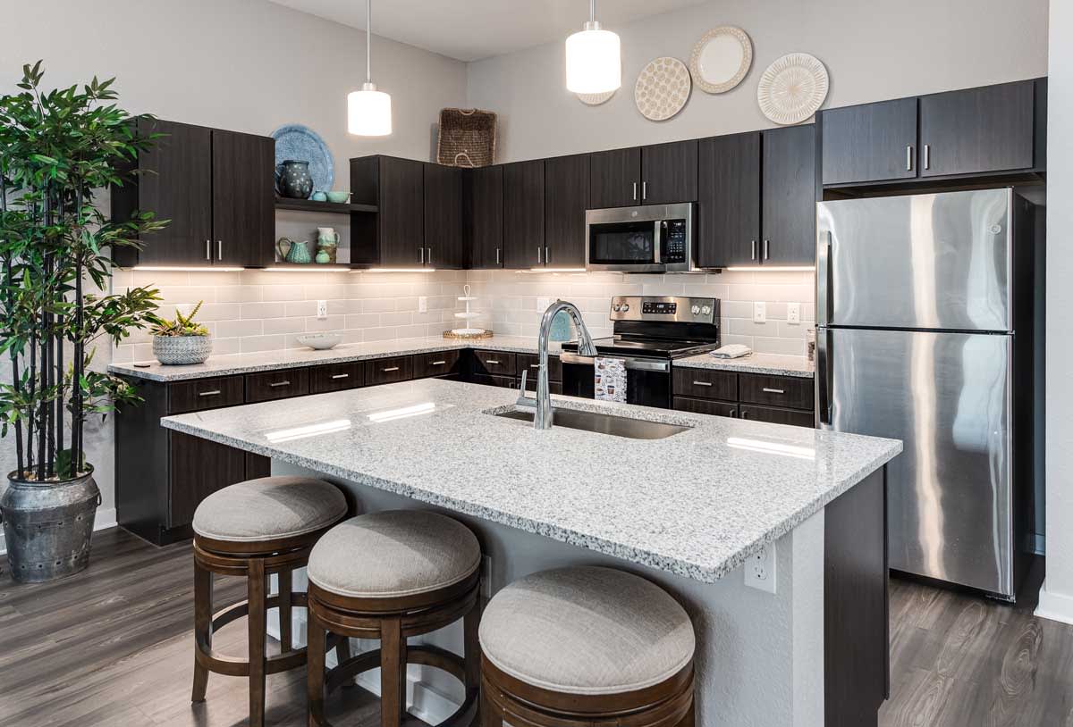 A modern kitchen with a central island, featuring dark cabinets and stainless steel appliances.