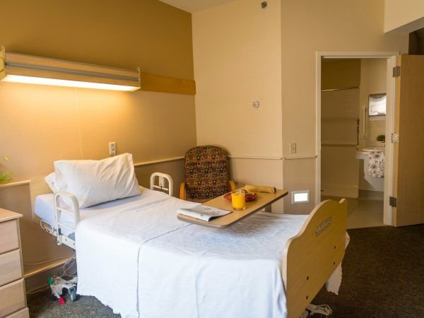 A tidy hospital room with a single bed and a small table for patients.